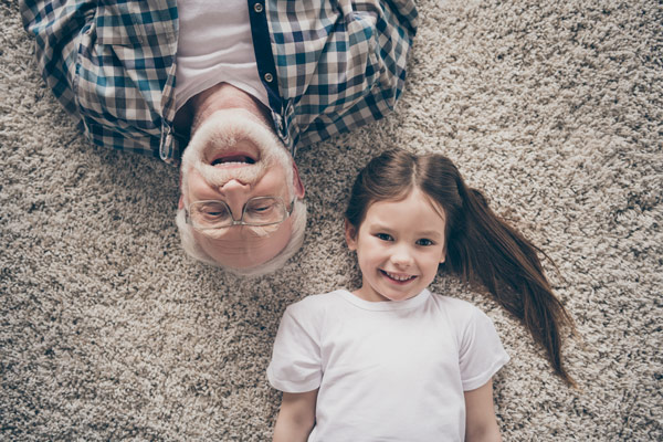 Grandad and Granddaughter laying on beige carpet smiling up at camera